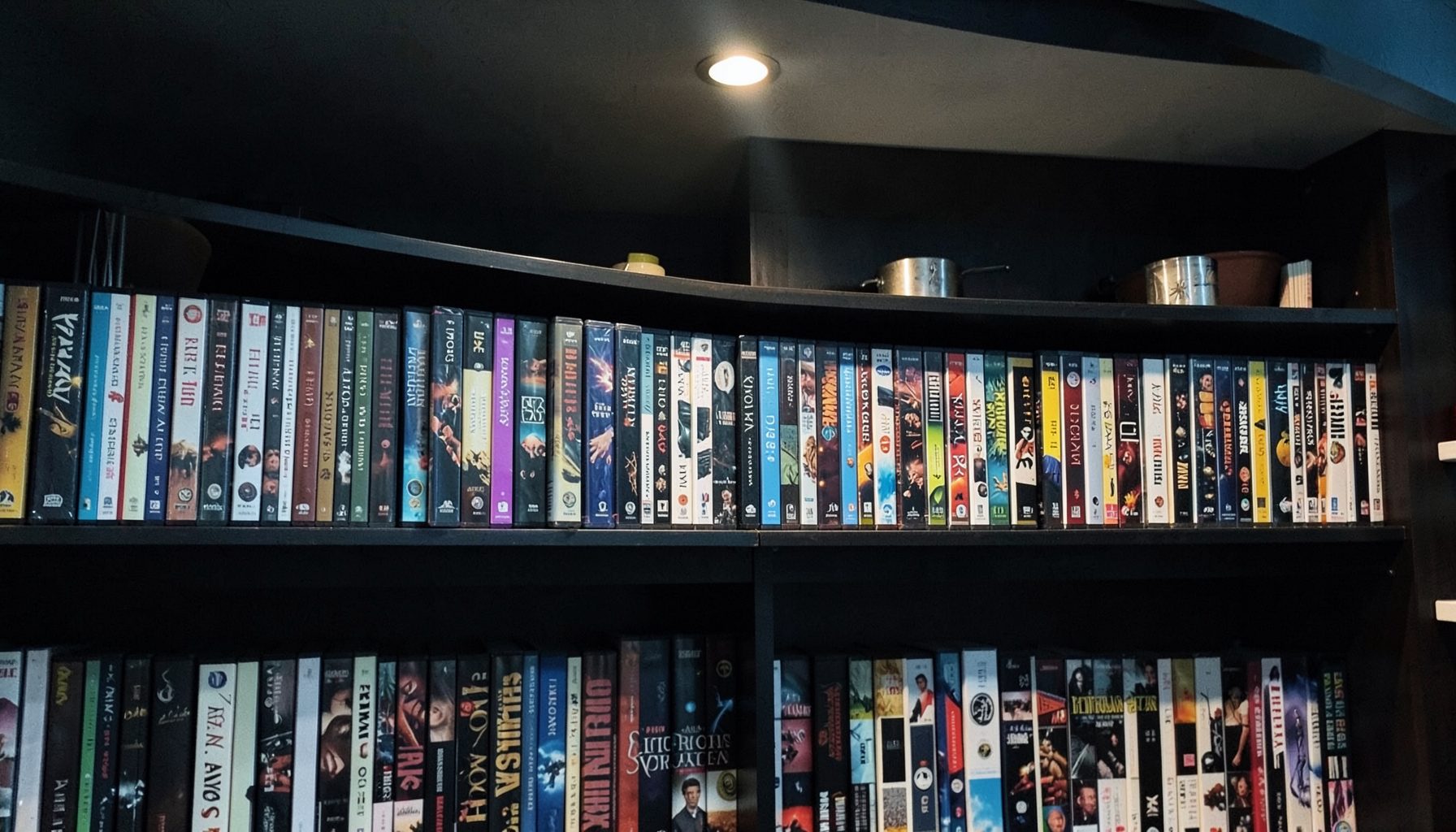 Rows of DVD cases organized by genre on dark shelving, soft overhead light, muted blues and warm wood tones